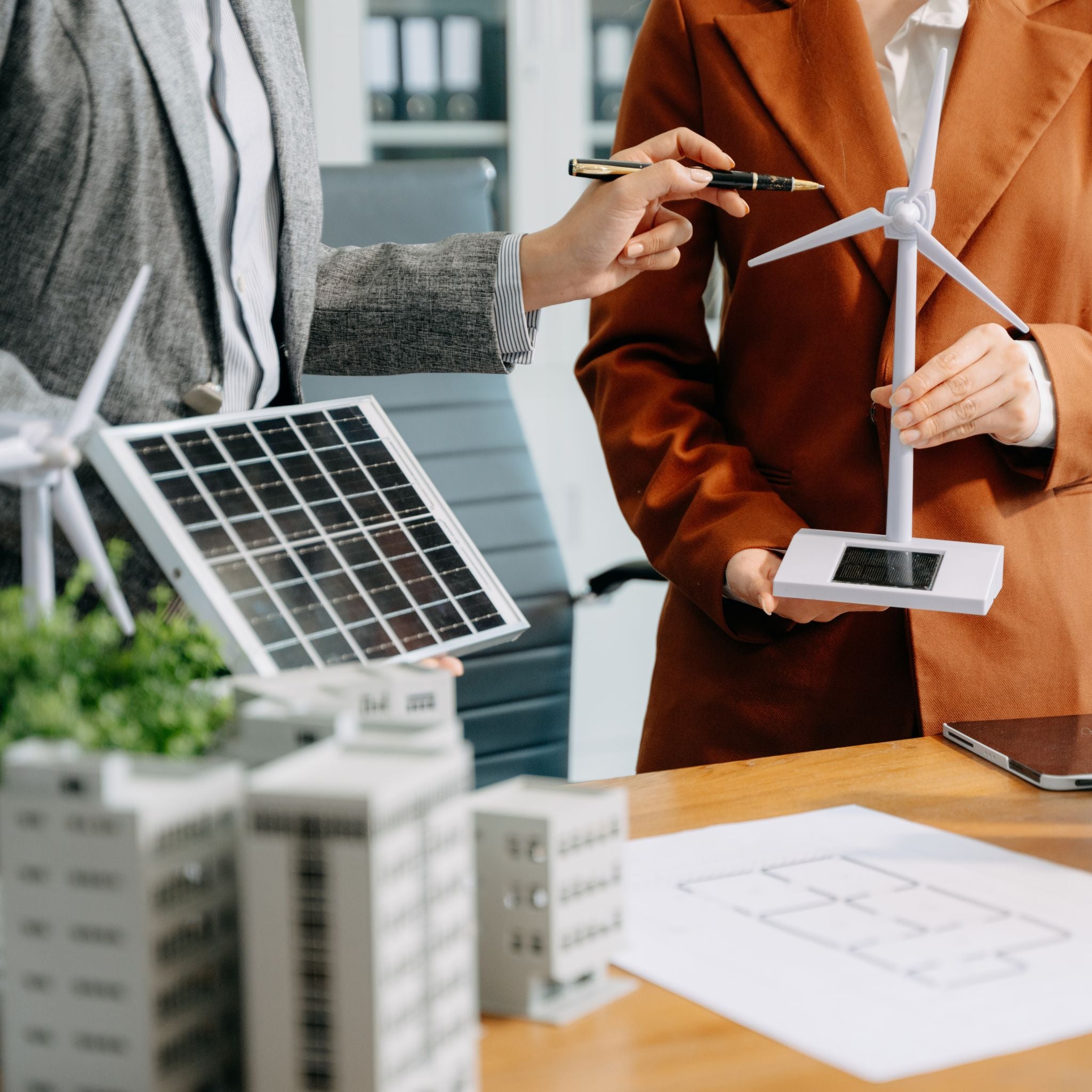 Two people discussing about a model of a wind turbine and solar panel 