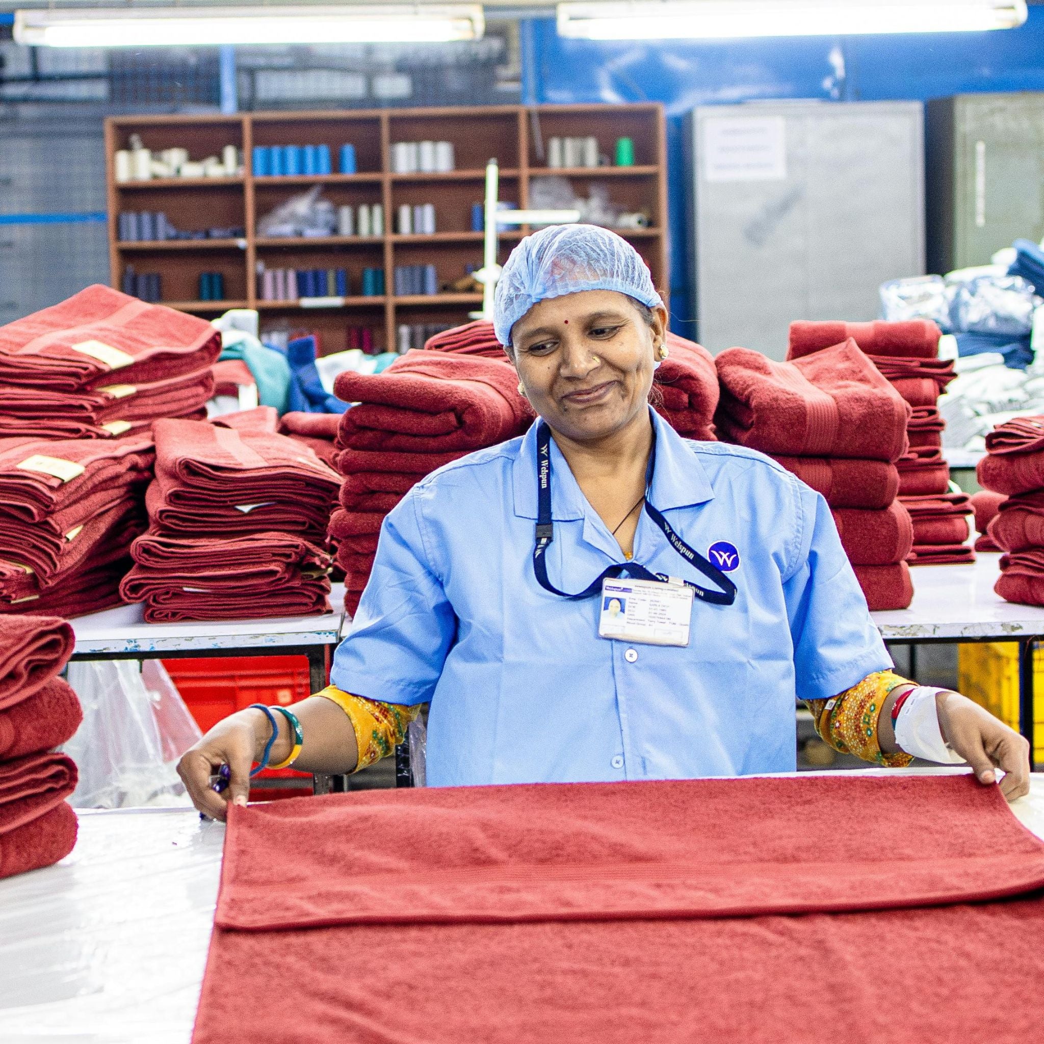 Worker in a blue uniform folding red fabric in a factory setting