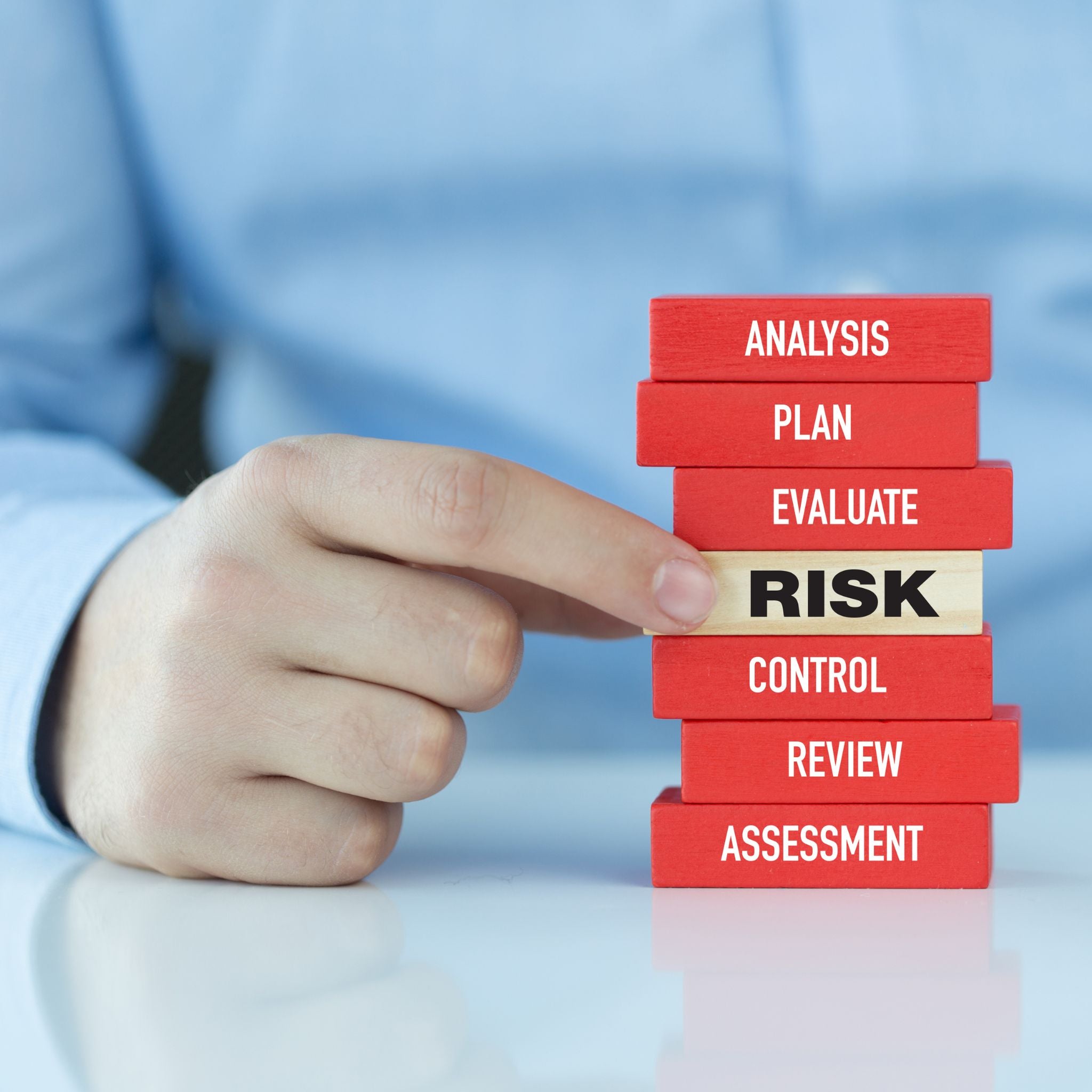 Hand placing a block labeled 'RISK' on a stack of risk management blocks 