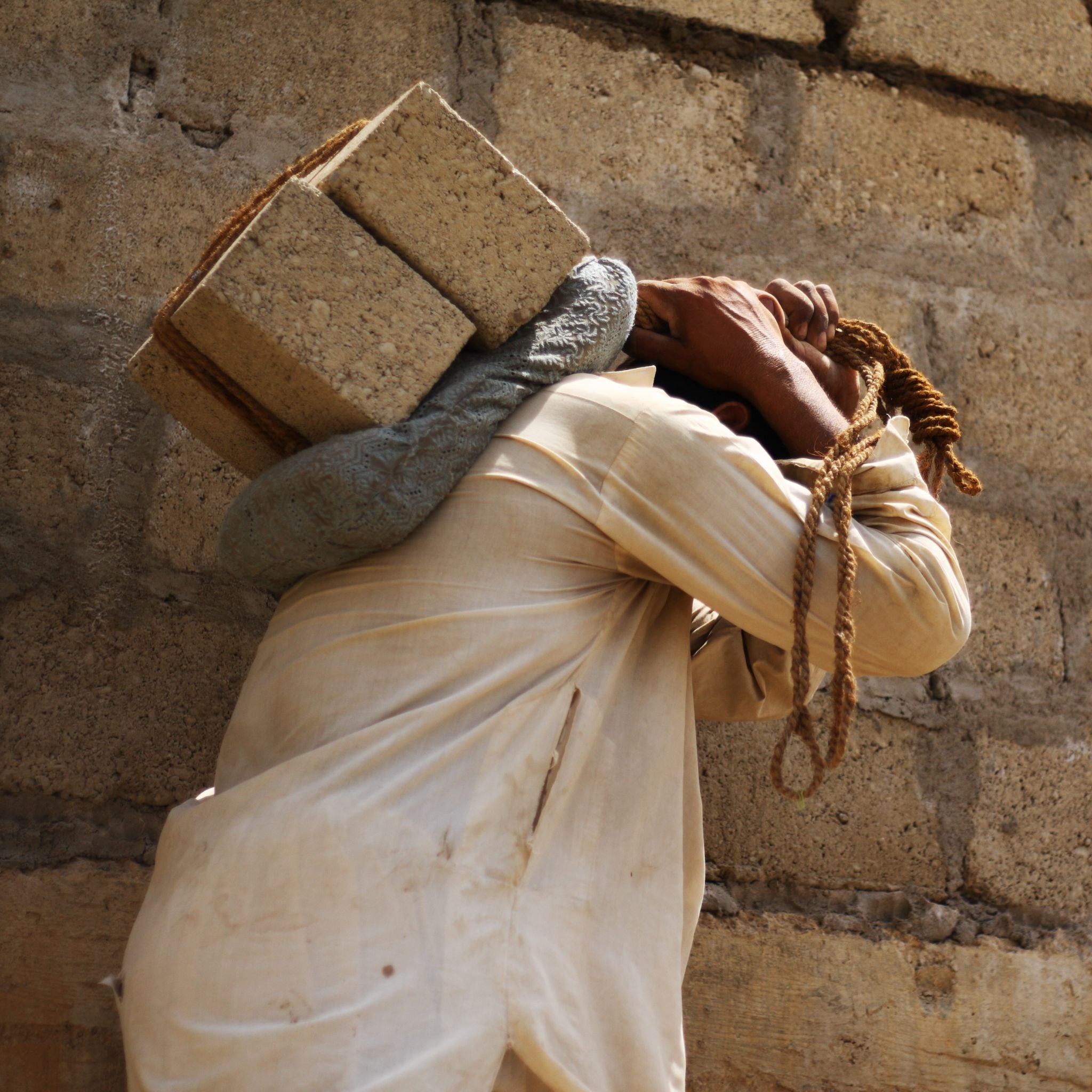 Person carrying bricks on their head against a stone wall