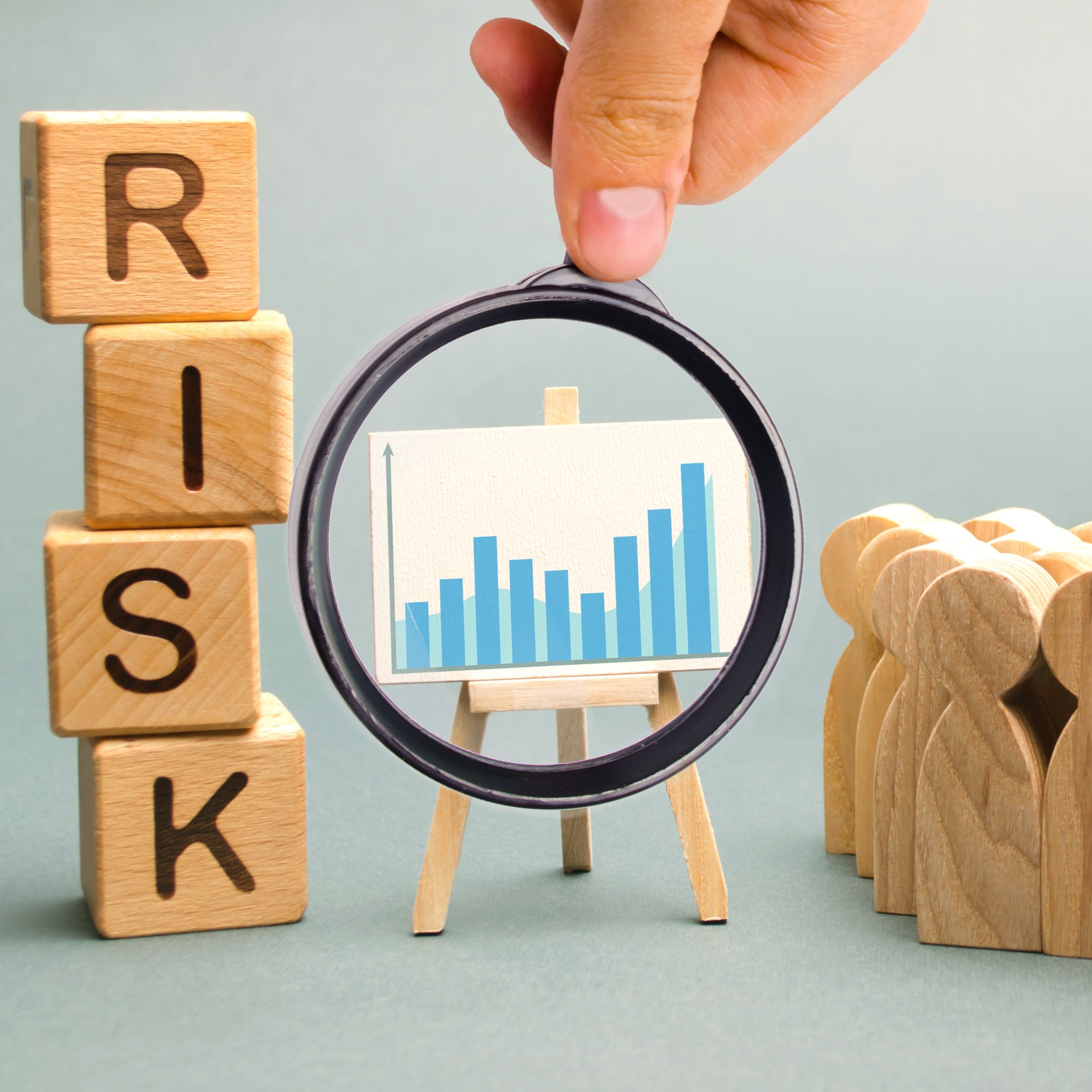 Wooden blocks spelling 'RISK', a hand holding a magnifying glass